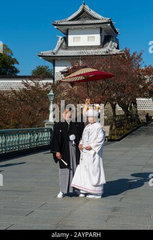 Un couple de mariage dans des vêtements traditionnels se pose devant le château du parc du château de Kanazawa à Kanazawa, préfecture d'Ishikawa, sur l'île d'Honshu Banque D'Images