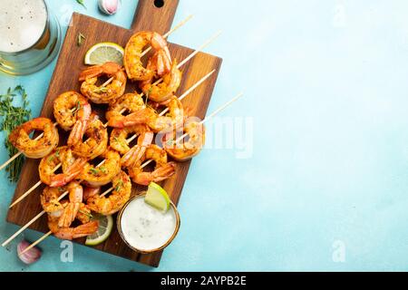 Brochettes de crevettes grillées ou langoustines servies avec de la chaux, de l'ail et de la sauce sur fond de béton bleu clair. Fruits de mer et bière. Vue de dessus avec copie Banque D'Images