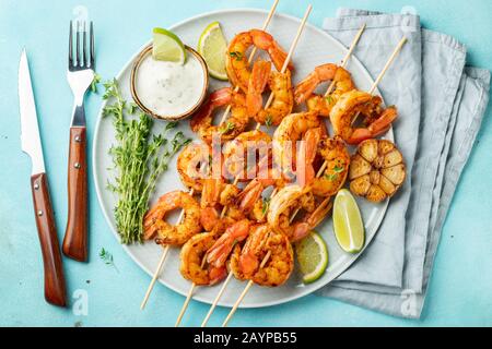 Brochettes de crevettes grillées ou langoustines servies avec de la chaux, de l'ail et de la sauce sur fond de béton bleu clair. Fruits de mer et bière. Vue de dessus. Pose à plat Banque D'Images