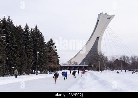 Montréal, CA - 15 février 2020 : patinage sur glace des gens à la patinoire du parc Maisonneuve avec la tour du stade olympique en arrière-plan. Banque D'Images