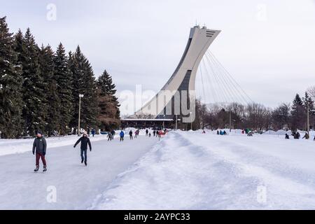 Montréal, CA - 15 février 2020 : patinage sur glace des gens à la patinoire du parc Maisonneuve avec la tour du stade olympique en arrière-plan. Banque D'Images