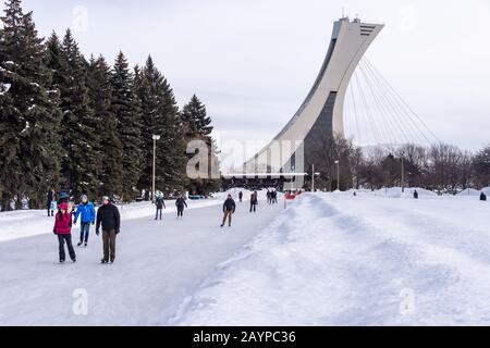 Montréal, CA - 15 février 2020 : patinage sur glace des gens à la patinoire du parc Maisonneuve avec la tour du stade olympique en arrière-plan. Banque D'Images