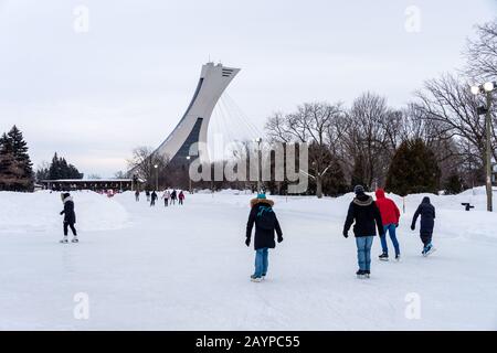 Montréal, CA - 15 février 2020 : patinage sur glace des gens à la patinoire du parc Maisonneuve avec la tour du stade olympique en arrière-plan. Banque D'Images