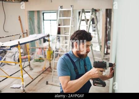 Portrait à grand angle du mur de forage du travailleur de la construction barbu tout en rénovant la maison seule, espace de copie Banque D'Images