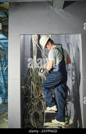 Vue arrière sur toute la longueur portrait des câbles de connexion des électriciens supérieurs dans l'armoire de câblage pendant la rénovation de la maison Banque D'Images