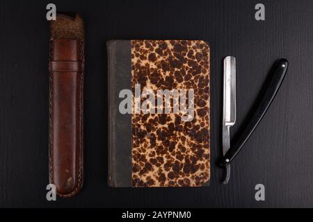 Rasoir et livre sur la table. Accessoires pour coiffeurs et littérature ancienne. Fond sombre. Banque D'Images