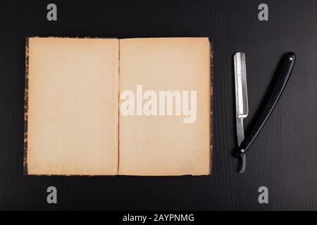 Rasoir et livre sur la table. Accessoires pour coiffeurs et littérature ancienne. Fond sombre. Banque D'Images