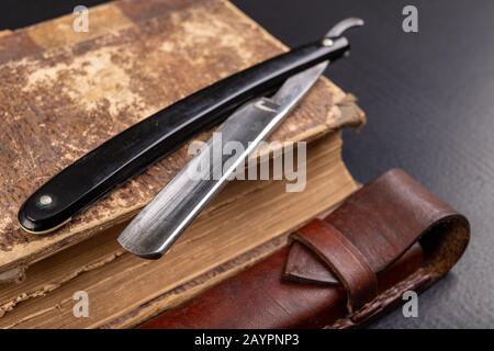 Rasoir et livre sur la table. Accessoires pour coiffeurs et littérature ancienne. Fond sombre. Banque D'Images