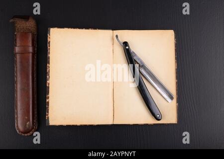 Rasoir et livre sur la table. Accessoires pour coiffeurs et littérature ancienne. Fond sombre. Banque D'Images