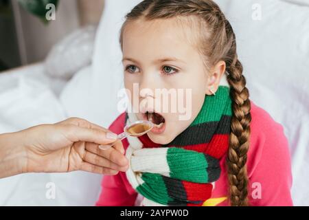 maman donnant du sirop à ma fille malade avec un foulard dans le lit Banque D'Images