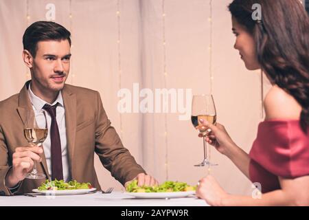 heureux, élégant homme et femme assis à la table servie et tenant vitré de vin blanc Banque D'Images