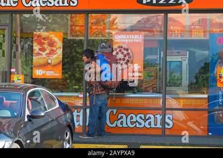 Jeune homme autochtone avec sac à dos devant Une Little Caesars Pizza, Vancouver, B. C., Canada. Banque D'Images