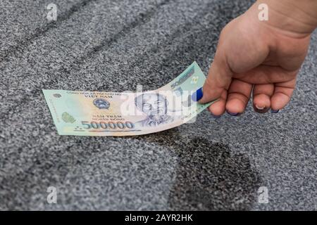 Une femme main gauche, des ongles bleus. Ramasse le billet d'argent vietnamien de 50000 dong sur le sol Banque D'Images