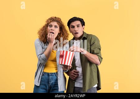 couple peur regardant un film d'horreur avec seau de pop-corn, isolé sur le jaune Banque D'Images