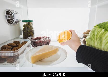 Vue rognée d'une femme prenant une tranche orange du réfrigérateur avec des aliments isolés sur blanc, image de stock Banque D'Images