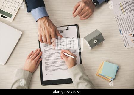 vue de dessus de l'agent pointant avec le doigt sur le presse-papiers avec lettrage de contrat près de la femme Banque D'Images