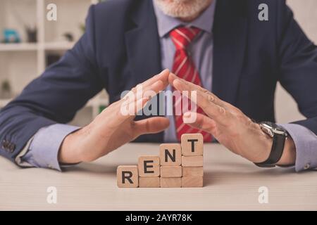 vue rognée de l'agent mettant les mains au-dessus des cubes en bois avec lettrage de loyer Banque D'Images