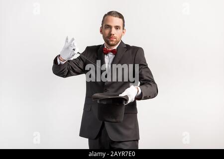 magicien en costume faisant un chapeau et une baguette de tour, isolé sur gris Banque D'Images