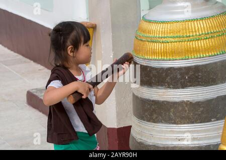 Une petite fille sonne une cloche (qui fait partie du rituel de prière) à la Pagode Shwedagon de 2 500 ans à Yangon (Rangoon), la plus grande ville du Myanmar. Banque D'Images