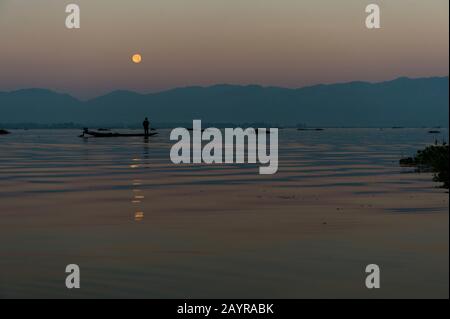 Avant le lever du soleil sous une pleine lune, un pêcheur d'aviron dans son bateau tire dans son filet de pêche il a mis la veille sur le lac Inle au Myanmar. Banque D'Images
