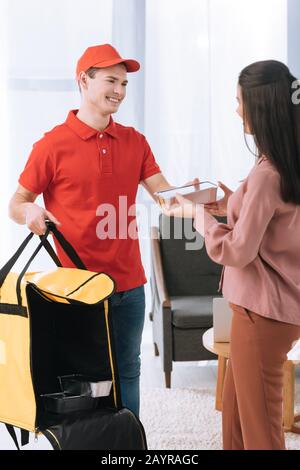 Homme souriant à la livraison avec sac thermo donnant un conteneur alimentaire à la femme à la maison Banque D'Images