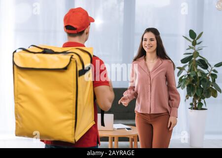 Objectif sélectif d'une femme d'affaires souriant par messagerie avec sac à dos thermo au bureau Banque D'Images