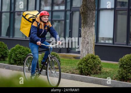 Objectif sélectif de l'homme souriant de livraison avec sac à dos thermo à vélo sur la rue urbaine Banque D'Images