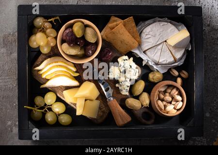 Vue de dessus des différents types de fromage avec fruits et noix autour du couteau sur le plateau sur fond gris Banque D'Images