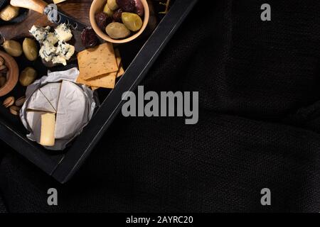 Vue de dessus du plateau avec des morceaux de camembert, dormlu, olives séchées, craquelins et pistaches isolés sur noir Banque D'Images