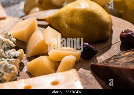 Foyer sélectif de différents types de fromage avec olives séchées et poire sur panneau rond en bois Banque D'Images