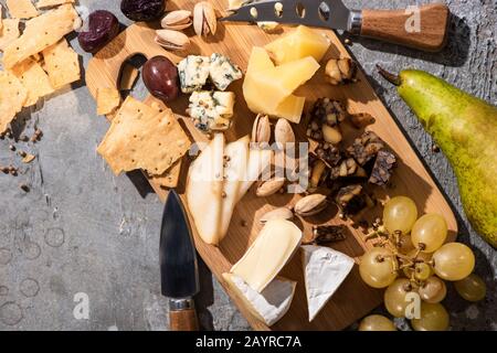 Vue de dessus des différents types de fromage avec olives séchées, pistaches, raisins, poires et crackers à bord de coupe Banque D'Images