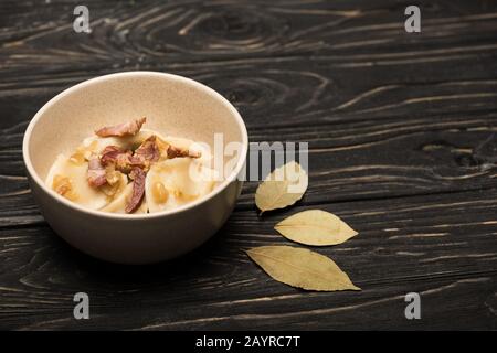 délicieux varenyky avec des crépitements dans un bol près des feuilles de laurier sur une table en bois noir Banque D'Images