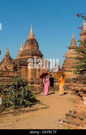 Un modèle de tournage avec deux jeunes femmes en robe traditionnelle et parasols dans un petit complexe de temple à Bagan, au Myanmar. Banque D'Images