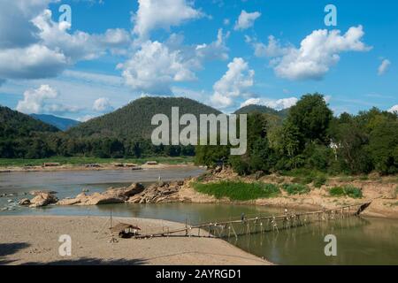 Vue sur un pont en bambou au-dessus du fleuve Nam Khan au confluent des rivières Nam Khan et Mékong à Luang Prabang au Laos central. Banque D'Images