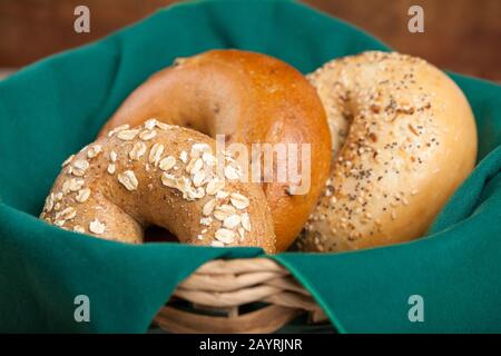 Trois variétés de bagels (grain entier, tourbillon de cannelle et raisins secs, et tout) reposant dans un panier à pain doublé de serviette Banque D'Images