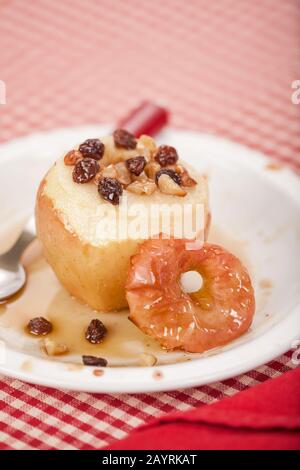 Pomme cuite au miel avec le noyau enlevé et rempli de raisins secs et de noix, et arrosée de miel, reposant sur une plaque de céramique blanche avec un caillot rouge Banque D'Images