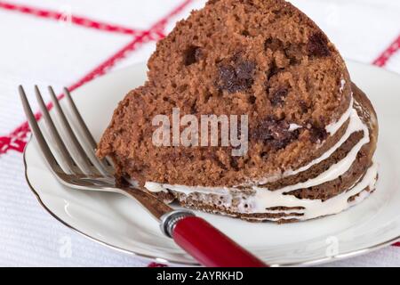 Tranche de gâteau de bundt au chocolat sur une plaque de chine, avec une fourchette à poignée rouge reposant à côté Banque D'Images
