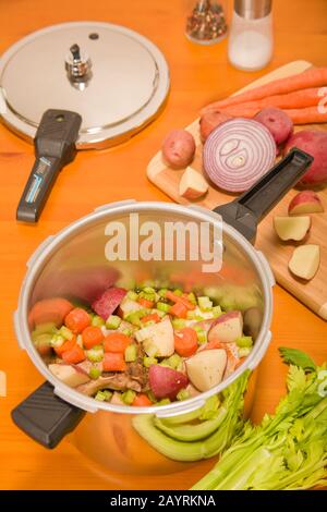 Côtelettes de porc et légumes crus dans un cuiseur sous pression, prêts à cuire, avec du céleri supplémentaire, des pommes de terre rouges, de l'oignon rouge, des carottes, du sel et du poivre assis à côté de moi Banque D'Images