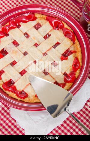 Tarte aux cerises cuite au four avec serveur à tarte sur une nappe en tissu à damier rouge et blanc avec une serviette en tissu à dentelle blanche Banque D'Images