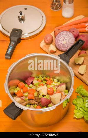 Côtelettes de porc et légumes crus dans un cuiseur sous pression, prêts à cuire, avec du céleri supplémentaire, des pommes de terre rouges, de l'oignon rouge, des carottes, du sel et du poivre assis à côté de moi Banque D'Images