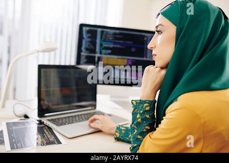 Belle jeune femme pensive dans le hijab traditionnel travaillant sur le code de programmation pour les étudiants projet Banque D'Images
