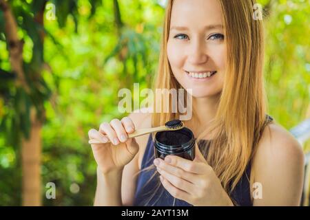 Jeune femme brosse les dents à l'aide de poudre De charbon Activée pour se brosser et blanchir les dents. Brosse écologique en bambou Banque D'Images