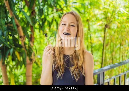 Jeune femme brosse les dents à l'aide de poudre De charbon Activée pour se brosser et blanchir les dents. Brosse écologique en bambou Banque D'Images