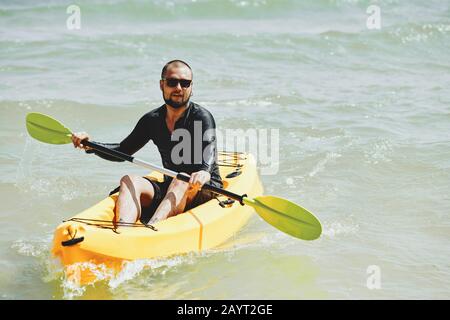 Installer un jeune homme dans un maillot à manches longues noires pagayant un kayak jaune en mer Banque D'Images