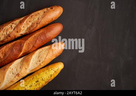 Trois baguettes françaises croustillantes sont noir foncé table fond graines de sésame traditionnel français pâtisseries Copier espace concept pour le menu ou la publicité Banque D'Images