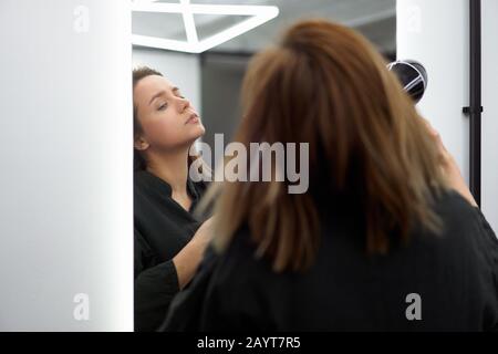 Portrait d'une belle femme caucasienne qui se tient près du miroir et sèche les cheveux avec un sèche-cheveux. Avec espace libre pour le texte Banque D'Images