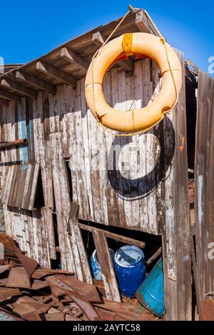 L'ancien économiseur de vie orange pendu sur le bord du toit du petit bâtiment en bois de merde parmi beaucoup de planches et ciel bleu clair Banque D'Images