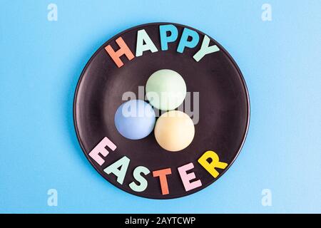 Joyeuses Pâques texte avec des œufs colorés disposés sur la plaque noire et fond bleu - vue de dessus Banque D'Images