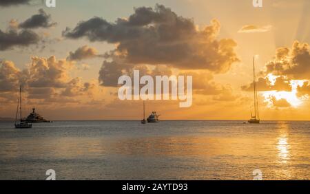 Vue sur le coucher du soleil des yachts ancrés dans la lagune, la baie Britannia, l'île Mustique, Saint-Vincent-et-les Grenadines, mer des Caraïbes Banque D'Images