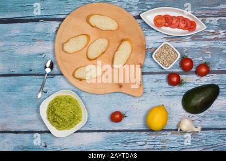 Ingrédients d'un sandwich à face ouverte avec de l'avocat étalé: Tomates cerises, amandes décortiquées de tournesol, avocat, citron, ail, morceaux de pain. Banque D'Images